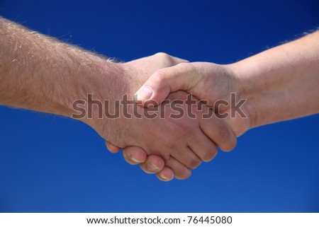 Two persons shaking hands in front of bright blue sky
