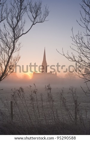 Dawn breaking through the mist revealing Salisbury cathedral.