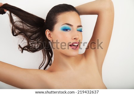 young beauty portrait with blue eye shadow and ponytail doing eye blink, studio white