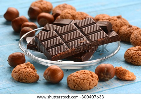 Chocolate tablet on glass dish with hazelnuts and biscuits around
