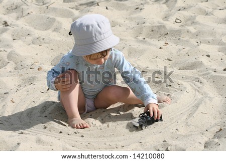 The boy on sand plays with the toy automobile