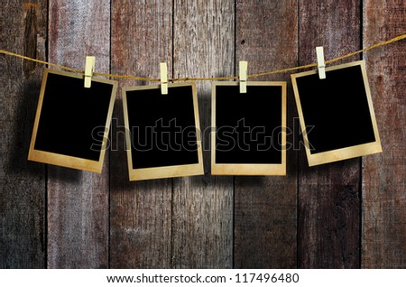 Old picture frame hanging on clothesline on wood background.