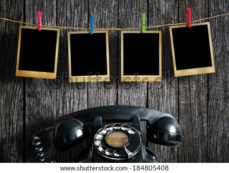 Old picture frame hanging on clothesline and old telephone on wood background.