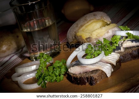 Sandwich with herring on rye bread, served with onion, jacket potato and glass of vodka