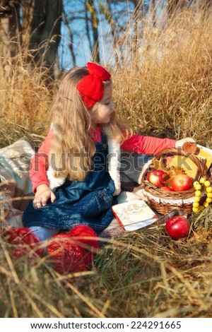 Little girl on nature with a basket of fruit and books