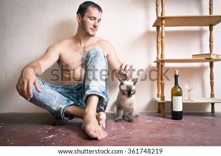 A man with a bottle of wine in his hand sitting on the floor near the cat