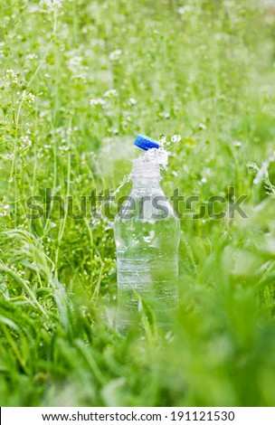 clean clear water splashing from a plastic bottle on the background of green grass