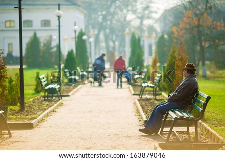 A lonely old man sitting on a bench in a park