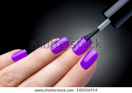 Beautiful manicure process. Nail polish being applied to hand, polish is a violet color. Black background closeup.
