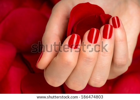 Beautiful female finger nails with red nail closeup on petals. Perfect manicure