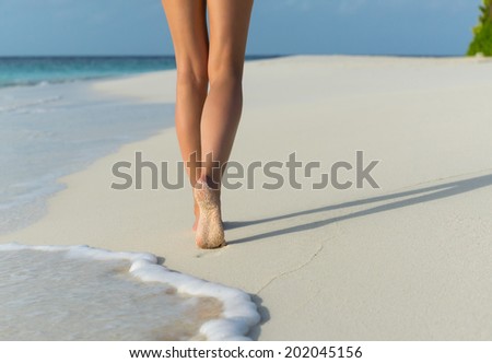 Beach travel - woman walking on sand beach leaving footprints in the sand. Closeup detail of female feet