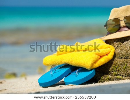 Straw hat, towel beach sun glasses and flip flops on a tropical beach
