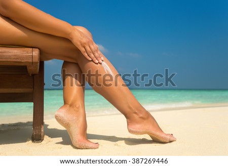 Woman applying sunblock cream on leg on beautiful tropical beach with white sand on summer vacation.