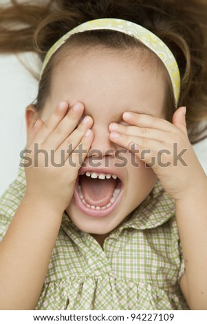Portrait of a laughing child who covers his face with his hands