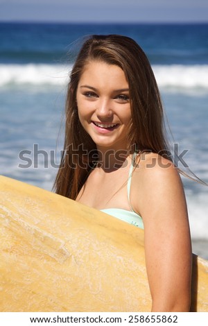 Beautiful Young Teenage Girl Holding a Surf Board at the Beach.  She is smiling