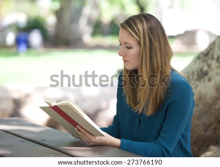 Beautiful Young Woman Reading a Book Outside at a park