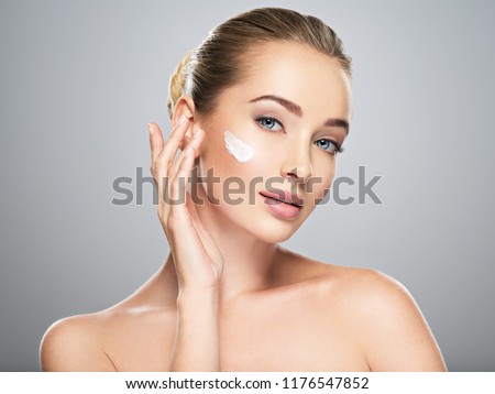 Beautiful young woman gets cream in the face. Skin care concept. Stunning caucasian woman with perfect health clean skin. Portrait of an Attractive girl  with blue eyes, closeup.