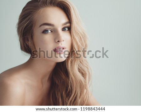 Young blond woman with long curly hair. Beautiful face of gorgeous girl with blue eyes. Nice portrait of a caucasian female looking at camera. Attractive fashion model