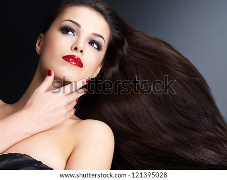 Beautiful woman with long brown straight hairs and red nails lying on the dark background