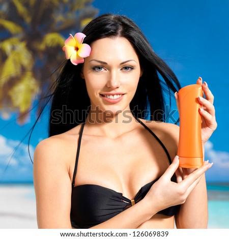 Portrait of  young happy woman on the beach  holds orange sun tan lotion bottle.