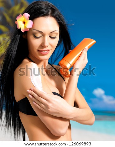 Beautiful young woman in black bikini applying sun block cream on the tanned body.  Girl  holding orange sun tan lotion bottle.