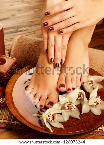 Closeup photo of a female feet at spa salon on pedicure procedure. Female legs in water decoration  the flowers.