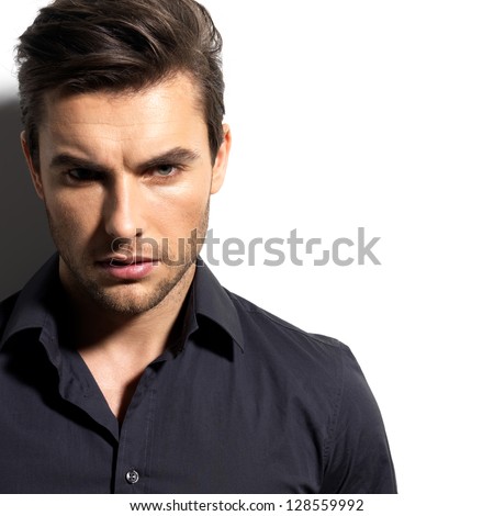 Fashion portrait of young man in black shirt poses over wall with contrast shadows - stock photo