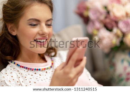 Happy young woman looking at her smart phone at home. Woman types message on her smart phone.