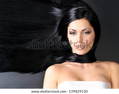 Portrait of a beautiful woman with long straight black hair lying on the dark background