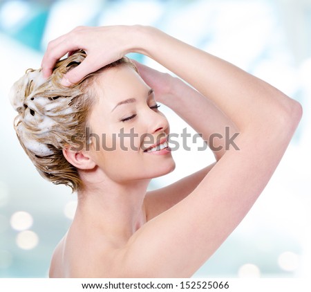 Beautiful young blond woman with attractive smile soaping her head - isolated on white background