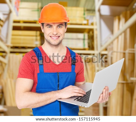 Portrait of smiling handyman with laptop working warehouse