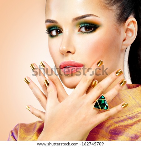 Glamour woman with beautiful golden nails and emerald ring on hands