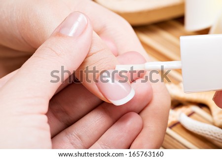 Woman in a nail salon receiving manicure. Beautician applying nail varnish on a thumbnail.