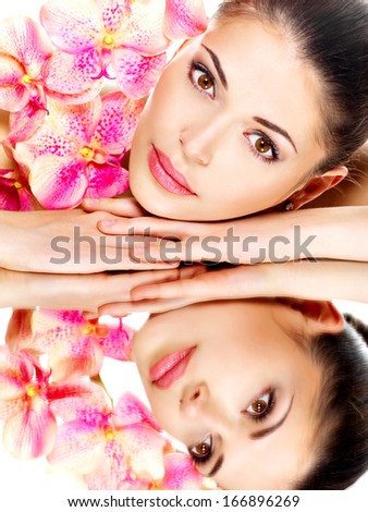 Portrait of a beautiful face of young pretty woman with healthy skin and pink flowers reflections in a mirror