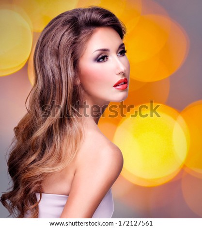 Beautiful sexy young woman with long wavy brown hair and red lips. Posing at studio over art lights