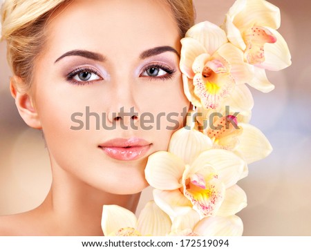 Young woman with health skin and flowers at face. Beauty treatment concept.