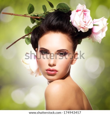 Beautiful woman with pink flowers in hairs posing over creative color background. Fashion model with creative hairstyle