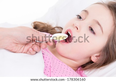 Little girl with sore throat lying in bed and using cough syrup on white background.