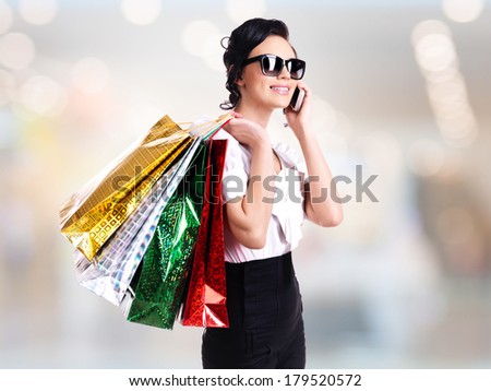 Portrait of smiling woman in sunglasses with shopping bags talking on the mobile phone in the shop.