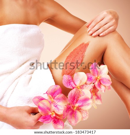 The woman with a beautiful body with flower using a scrub on her leg - studio