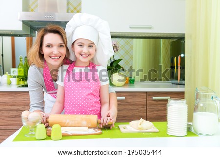 Attractive happy mother and daughter baking together at the kitchen.