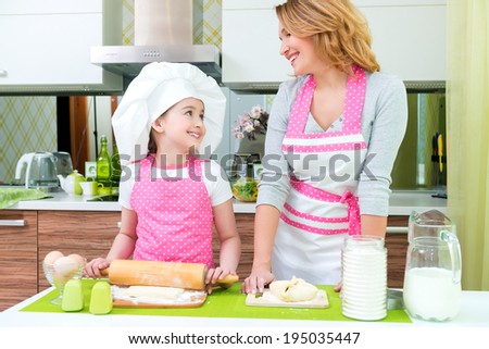Portrait of happy smiling mother and daughter making pies together at the kitchen.