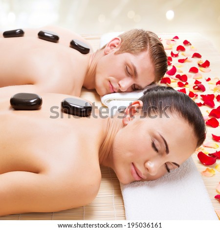 Portrait of attractive couple relaxing in spa salon with hot stones on body.