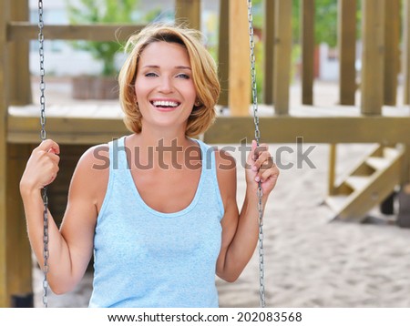 Portrait of happy beautiful woman having fun on a swing in a summer park.