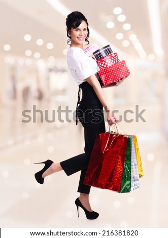 Full portrait of happy woman with color shopping bags and boxes standing in the shop.