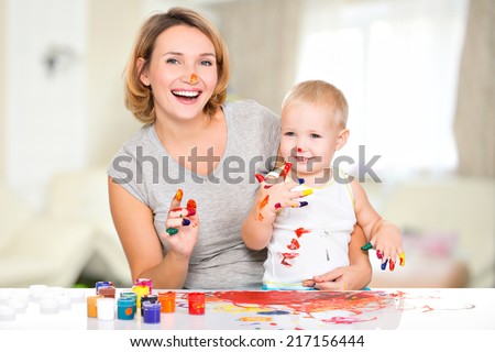 Happy child draws on the face of his mother -  indoors.