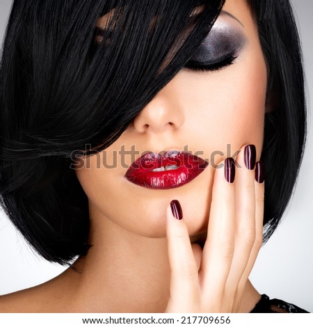 Face of a woman with beautiful dark nails and sexy red lips. Fashion model with black shot hairs at studio