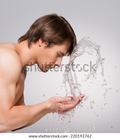 Profile portrait of a handsome man washing his face with water on gray background.