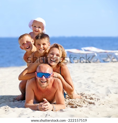 Happy mother and father with three children lying on the sunny beach.