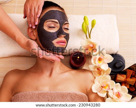 Cosmetologist doing massage on the woman's face  in sap salon. Female with scrub cosmetic mask on face.